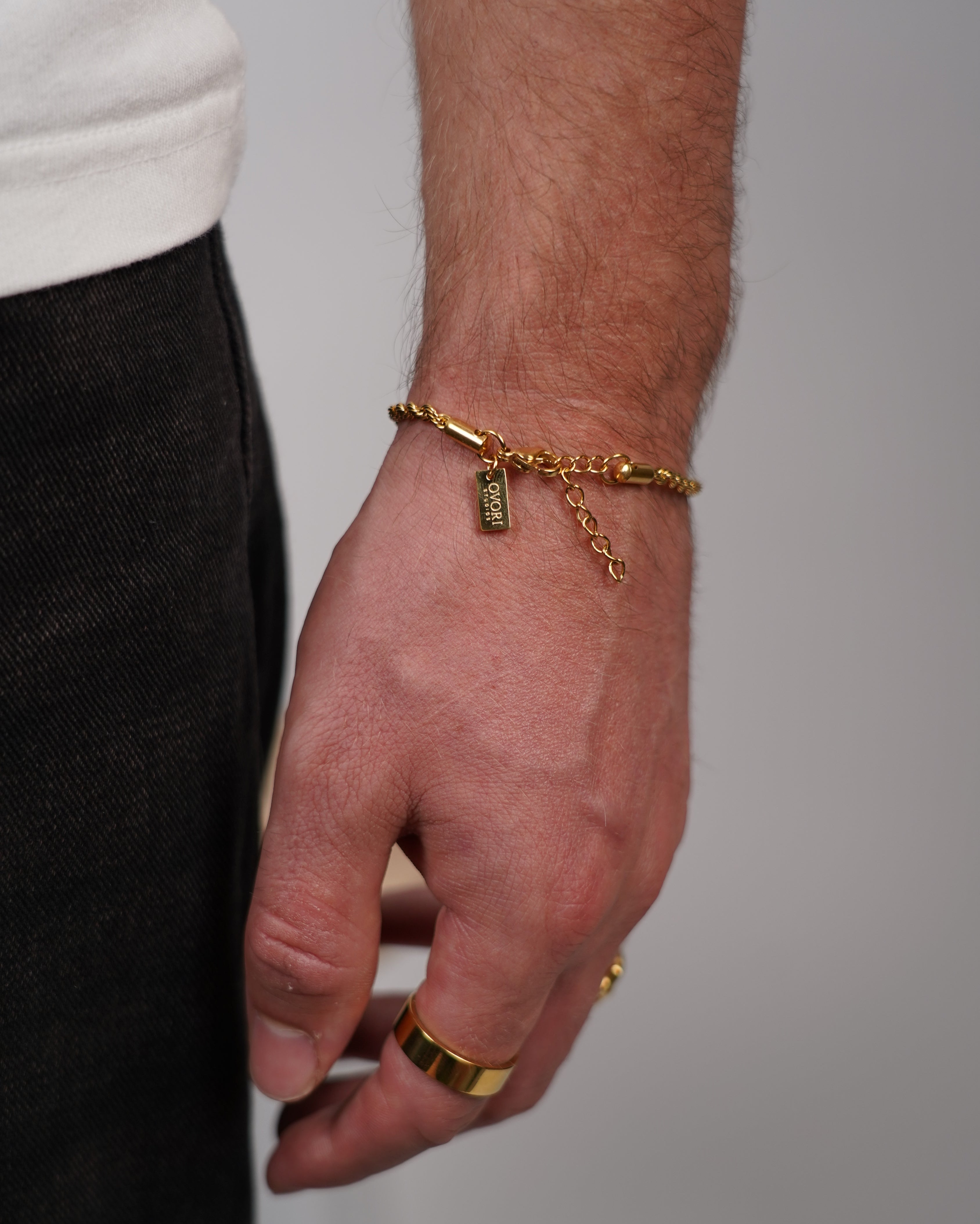 Hand wearing a gold ring and bracelet on a neutral background
